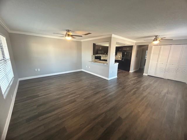 unfurnished living room with ceiling fan, crown molding, and dark wood-type flooring