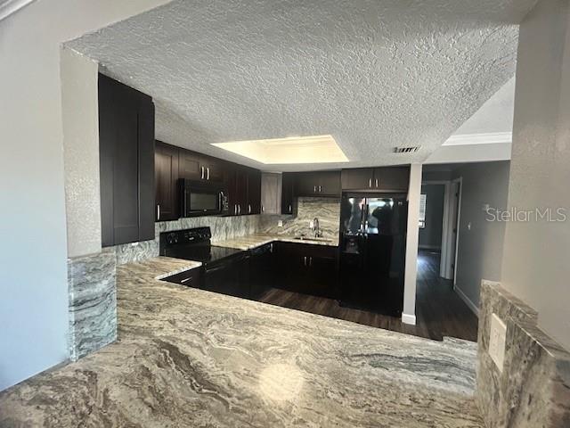 kitchen with tasteful backsplash, dark hardwood / wood-style floors, a textured ceiling, dark brown cabinets, and black appliances