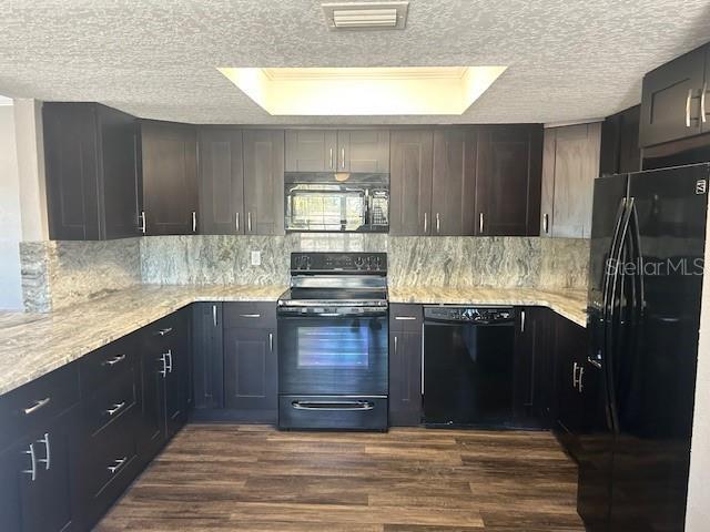 kitchen featuring black appliances, dark hardwood / wood-style floors, a raised ceiling, and dark brown cabinetry