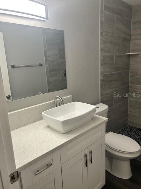 bathroom featuring vanity, toilet, and a tile shower