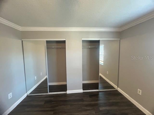 unfurnished bedroom featuring multiple closets, dark hardwood / wood-style flooring, a textured ceiling, and ornamental molding