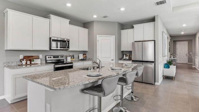 kitchen with white cabinets, sink, stainless steel appliances, and an island with sink