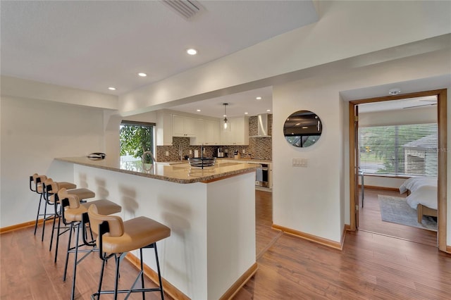 kitchen featuring kitchen peninsula, light stone countertops, a healthy amount of sunlight, pendant lighting, and white cabinetry