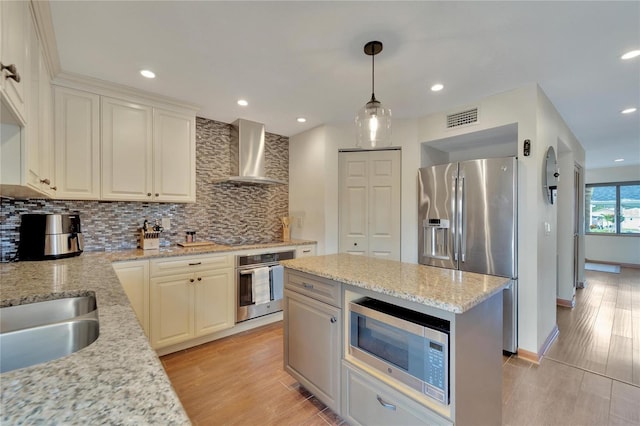 kitchen featuring hanging light fixtures, wall chimney exhaust hood, decorative backsplash, appliances with stainless steel finishes, and light stone counters