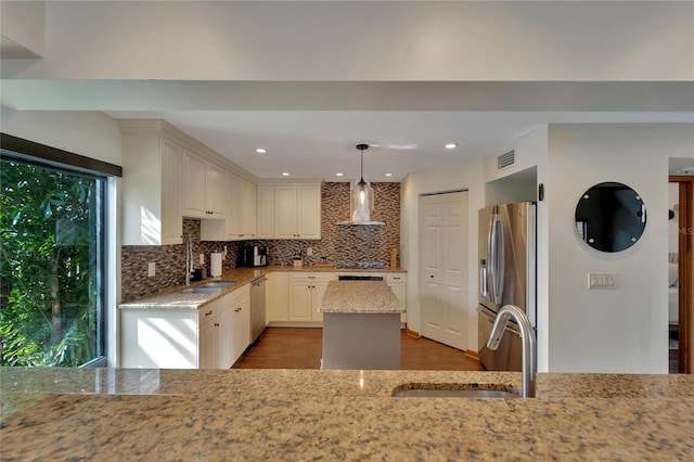 kitchen with light stone counters, stainless steel appliances, sink, wall chimney range hood, and decorative light fixtures