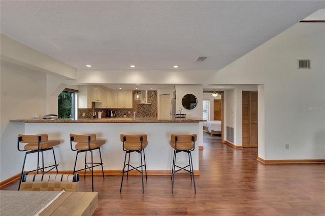 kitchen with a kitchen breakfast bar, kitchen peninsula, dark hardwood / wood-style floors, tasteful backsplash, and white cabinetry