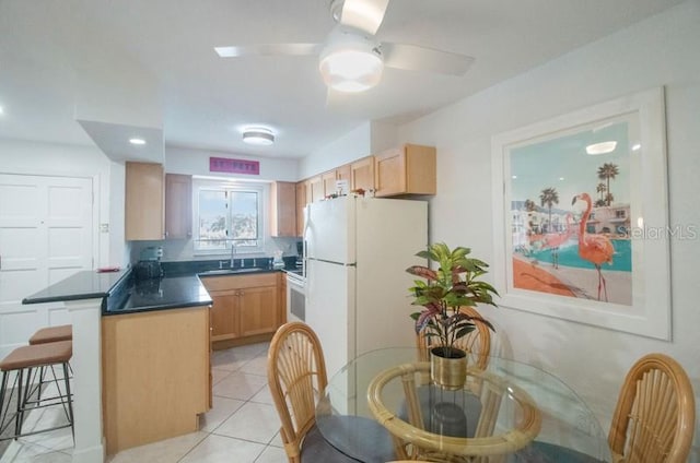 kitchen with ceiling fan, sink, white fridge, a breakfast bar area, and light brown cabinetry