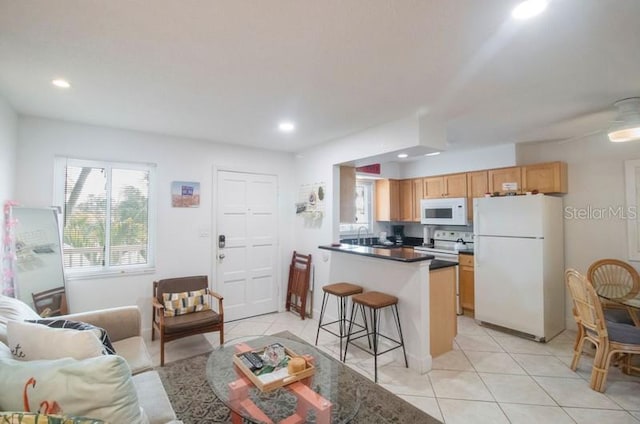 kitchen with a kitchen bar, kitchen peninsula, light tile patterned floors, and white appliances