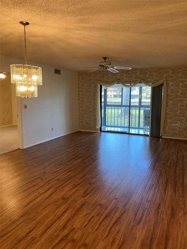 spare room with a textured ceiling, ceiling fan with notable chandelier, and dark wood-type flooring