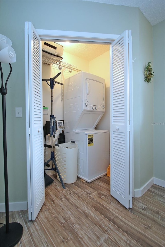 laundry area with a textured ceiling, light wood-type flooring, and stacked washer and dryer