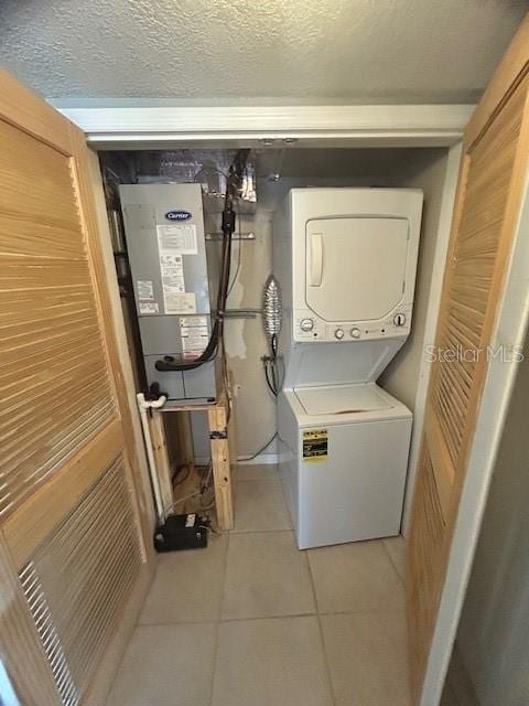 laundry room featuring a textured ceiling, light tile patterned floors, and stacked washer and dryer