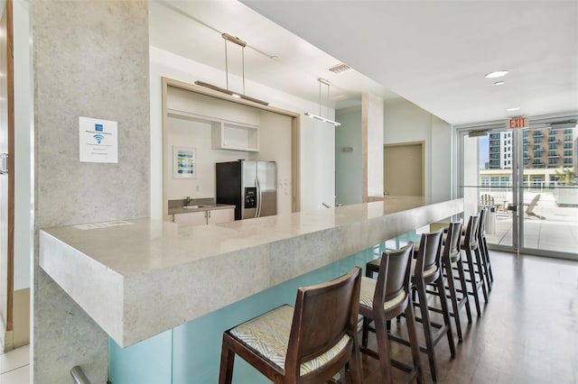 kitchen featuring floor to ceiling windows, stainless steel fridge, a kitchen bar, and decorative light fixtures