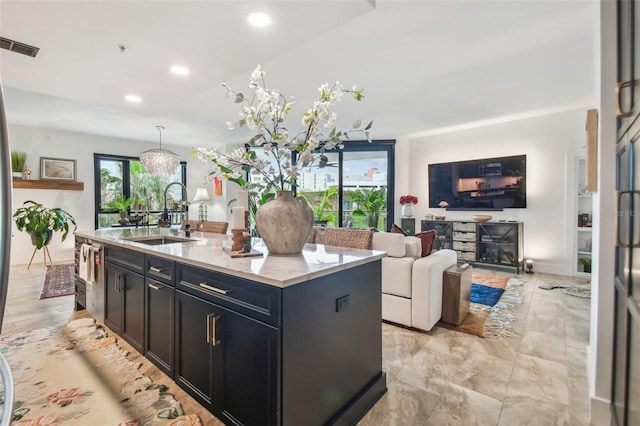 kitchen with an island with sink, light stone countertops, sink, and decorative light fixtures