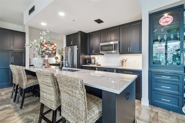 kitchen with sink, a breakfast bar area, light stone counters, appliances with stainless steel finishes, and a kitchen island with sink