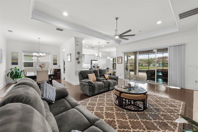 living room with ceiling fan with notable chandelier, dark hardwood / wood-style flooring, ornamental molding, and a tray ceiling