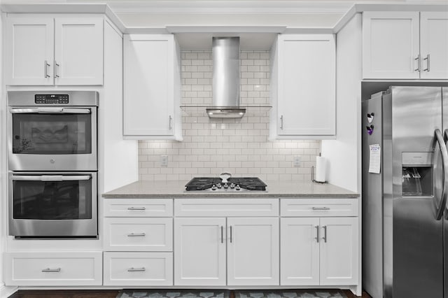 kitchen featuring appliances with stainless steel finishes, tasteful backsplash, light stone counters, wall chimney range hood, and white cabinets