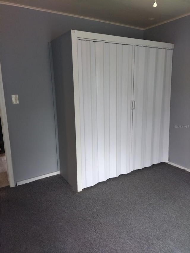 unfurnished bedroom featuring dark colored carpet, a closet, and crown molding