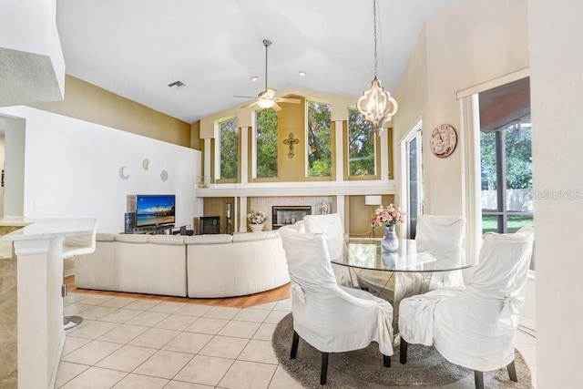 dining area with a tile fireplace, ceiling fan, light tile patterned floors, and high vaulted ceiling