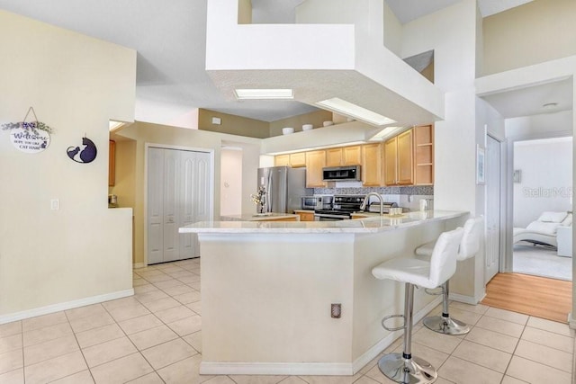 kitchen with a breakfast bar, light tile patterned floors, kitchen peninsula, and appliances with stainless steel finishes