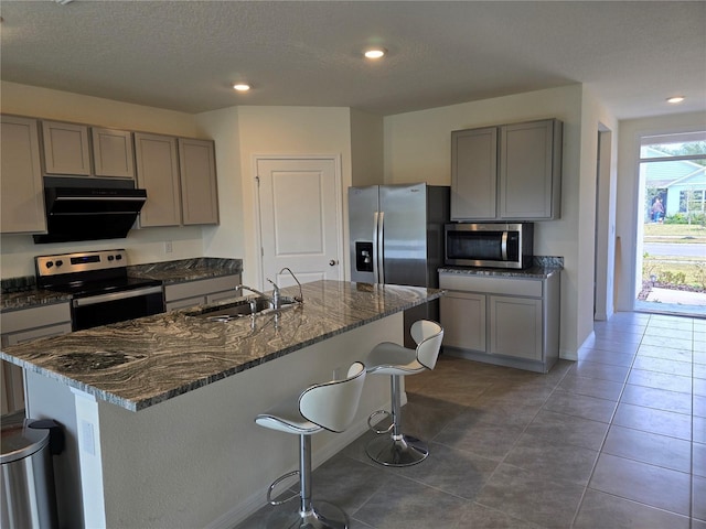 kitchen with a kitchen island with sink, ventilation hood, sink, dark stone countertops, and stainless steel appliances