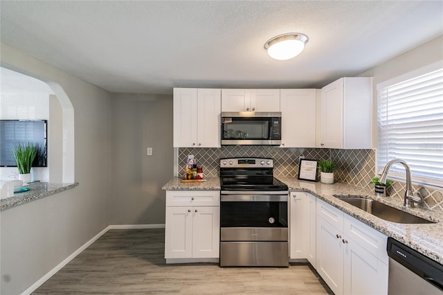 kitchen with light stone countertops, stainless steel appliances, white cabinetry, and sink