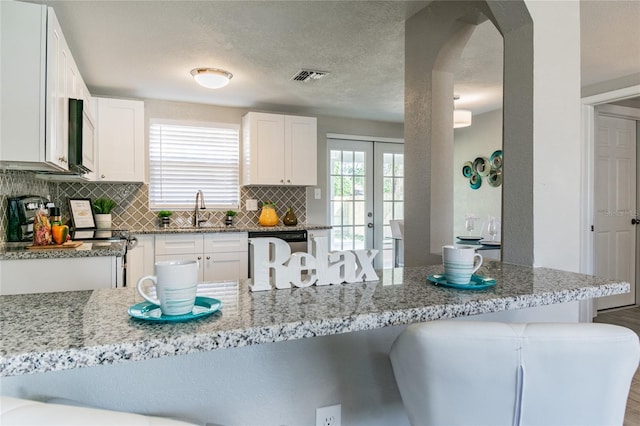 kitchen with white cabinetry, sink, backsplash, white dishwasher, and a breakfast bar