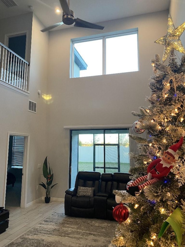 living room with plenty of natural light, ceiling fan, wood-type flooring, and a towering ceiling