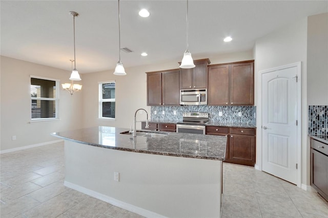 kitchen with sink, stainless steel appliances, backsplash, decorative light fixtures, and a kitchen island with sink