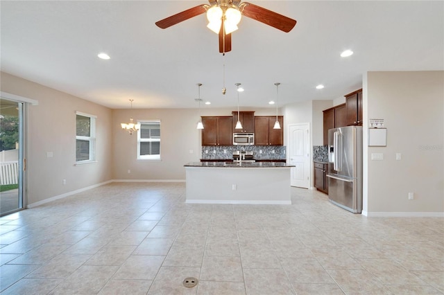 kitchen with pendant lighting, backsplash, ceiling fan with notable chandelier, an island with sink, and appliances with stainless steel finishes