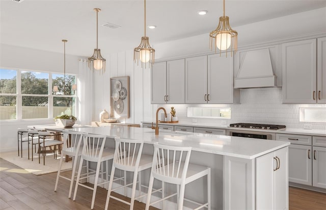 kitchen with premium range hood, pendant lighting, a center island with sink, and hardwood / wood-style floors