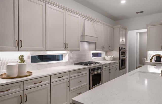 kitchen featuring custom exhaust hood, sink, light stone countertops, tasteful backsplash, and stainless steel appliances