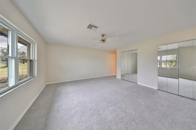 unfurnished bedroom with carpet flooring, ceiling fan, and multiple closets