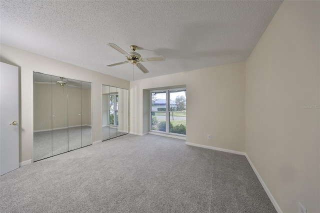 unfurnished bedroom featuring carpet flooring, ceiling fan, a textured ceiling, and two closets