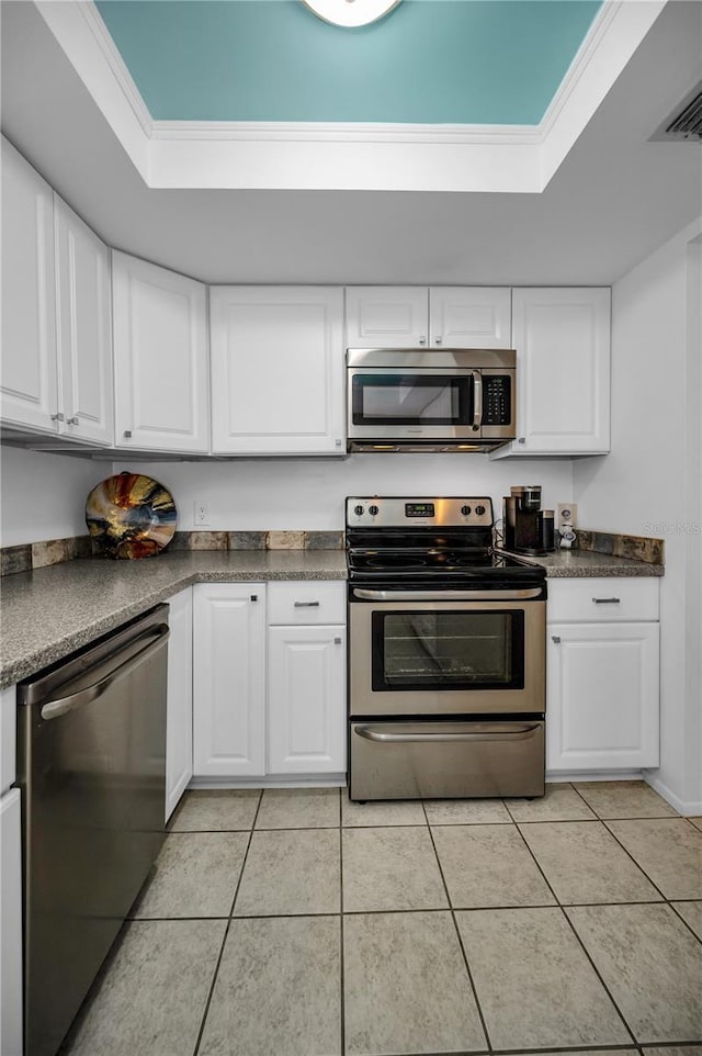 kitchen with appliances with stainless steel finishes, white cabinets, ornamental molding, light tile patterned floors, and a tray ceiling