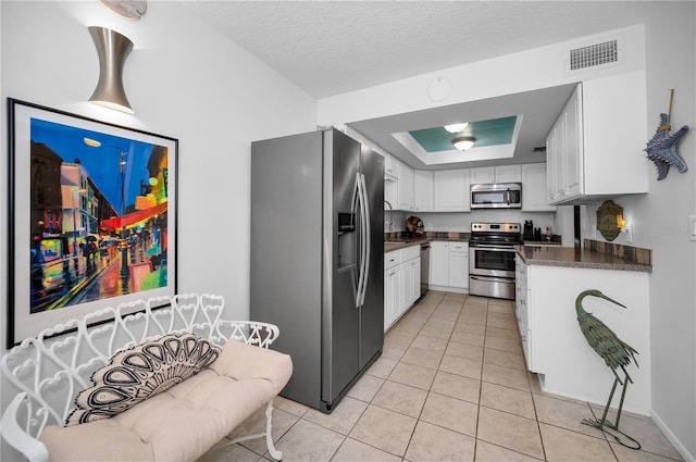 kitchen featuring light tile patterned flooring, a textured ceiling, a raised ceiling, stainless steel appliances, and white cabinets