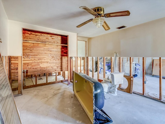 misc room featuring concrete floors, ceiling fan, and wood walls