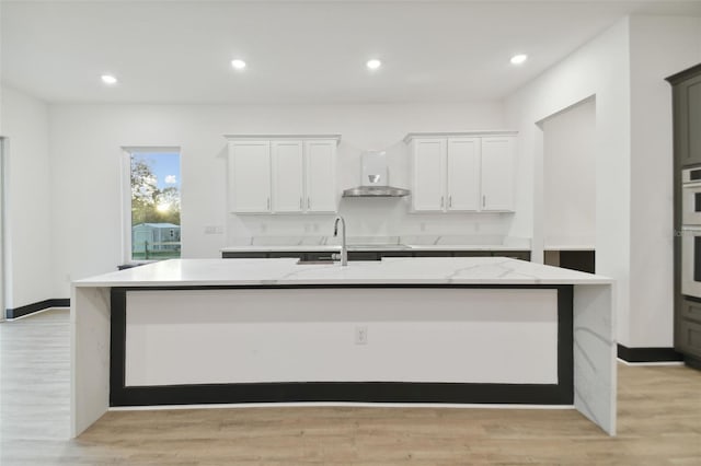 kitchen with white cabinets, light hardwood / wood-style flooring, a spacious island, and wall chimney range hood