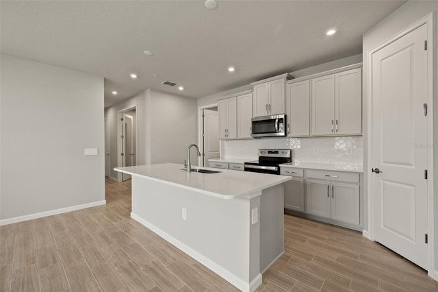 kitchen with sink, gray cabinets, a kitchen island with sink, stainless steel appliances, and decorative backsplash