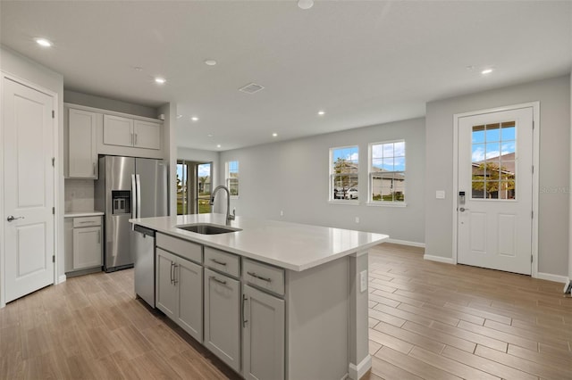 kitchen with an island with sink, appliances with stainless steel finishes, sink, and gray cabinetry