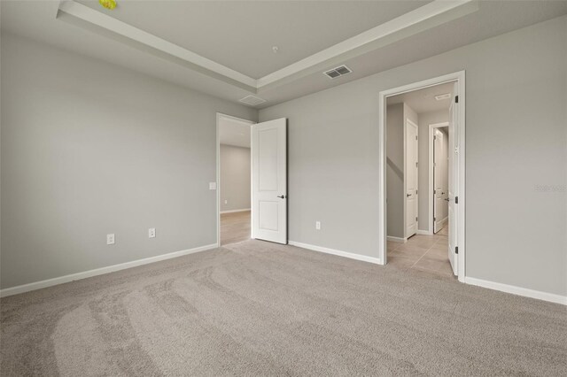 unfurnished bedroom featuring a raised ceiling and light carpet