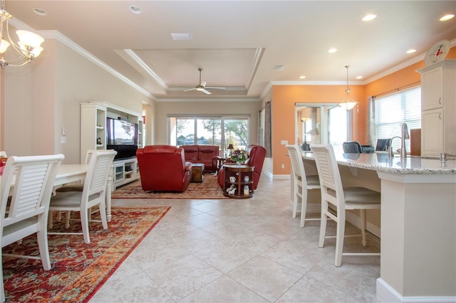 tiled dining space featuring ceiling fan with notable chandelier, a healthy amount of sunlight, a raised ceiling, and crown molding