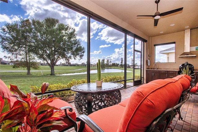 sunroom / solarium with a water view, ceiling fan, and sink