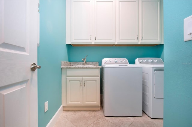 clothes washing area with washing machine and dryer, sink, light tile patterned floors, and cabinets