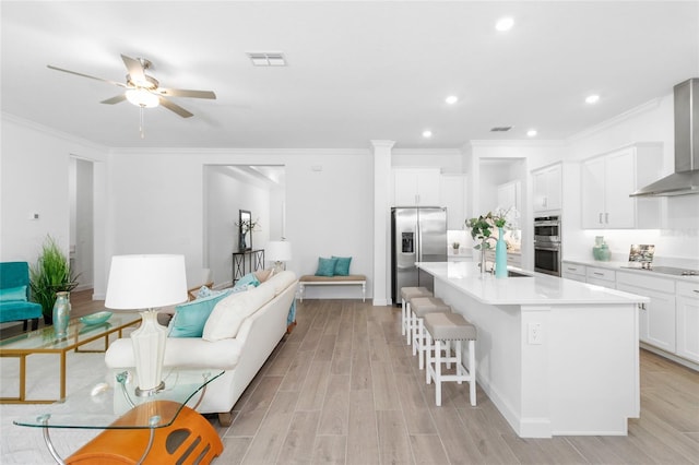 kitchen featuring a center island with sink, stainless steel appliances, a breakfast bar, white cabinets, and wall chimney exhaust hood