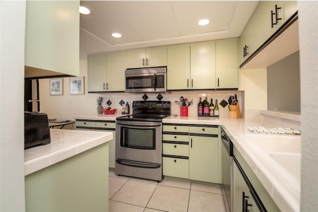 kitchen with appliances with stainless steel finishes, light tile patterned floors, and green cabinetry