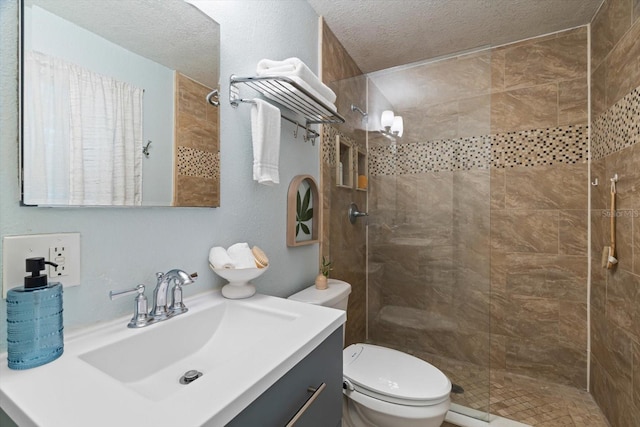 bathroom featuring a tile shower, vanity, a textured ceiling, and toilet