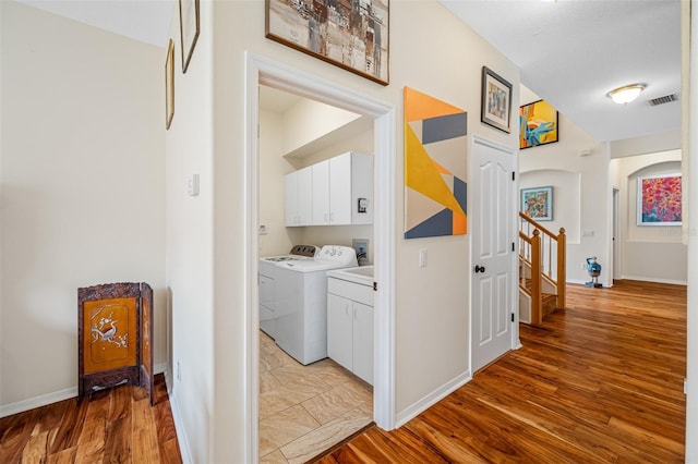 clothes washing area featuring cabinets, washing machine and clothes dryer, a textured ceiling, and light hardwood / wood-style flooring