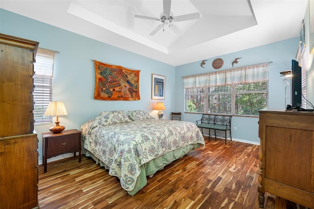 bedroom featuring hardwood / wood-style floors, a tray ceiling, multiple windows, and ceiling fan