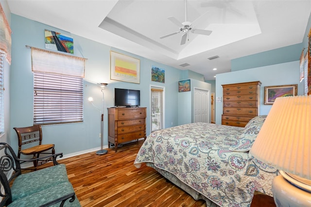 bedroom with a raised ceiling, ceiling fan, a closet, and hardwood / wood-style floors