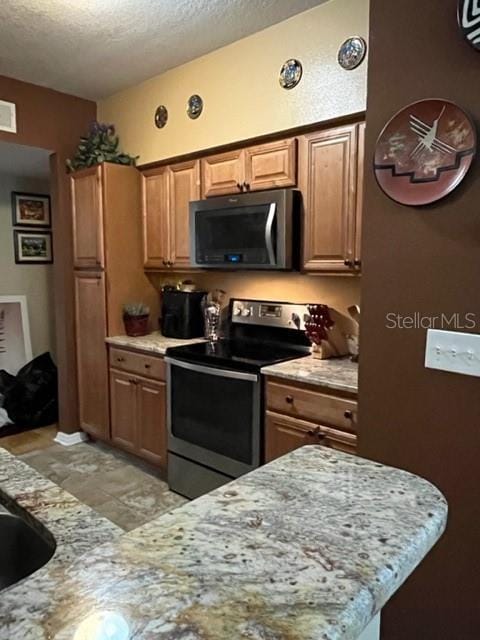 kitchen featuring light stone countertops, a textured ceiling, and stainless steel electric range